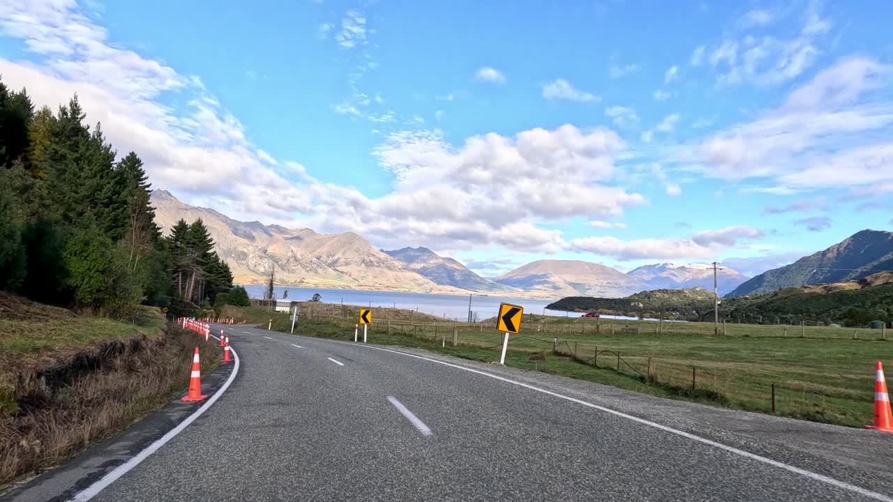 A picturesque drive along winding roads in Queenstown, New Zealand, showcasing lush landscapes and mountain views under clear skies