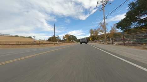 Street-view-of-vehicle-traveling-down-country-rural-paved-road-on-sunny-day