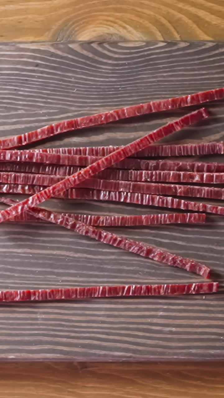 Man hands drop delicious sun-dried red fish salmon sticks onto rustic wooden cutting board in light room close view from above slow motion