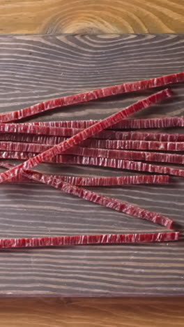 man hands drop delicious sun-dried red fish salmon sticks onto rustic wooden cutting board in light room close view from above slow motion
