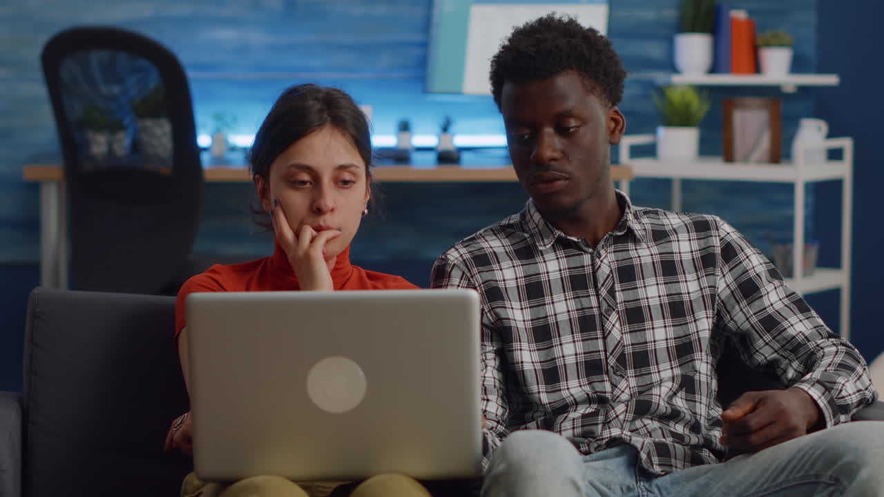 Interracial couple looking at laptop and sitting on sofa