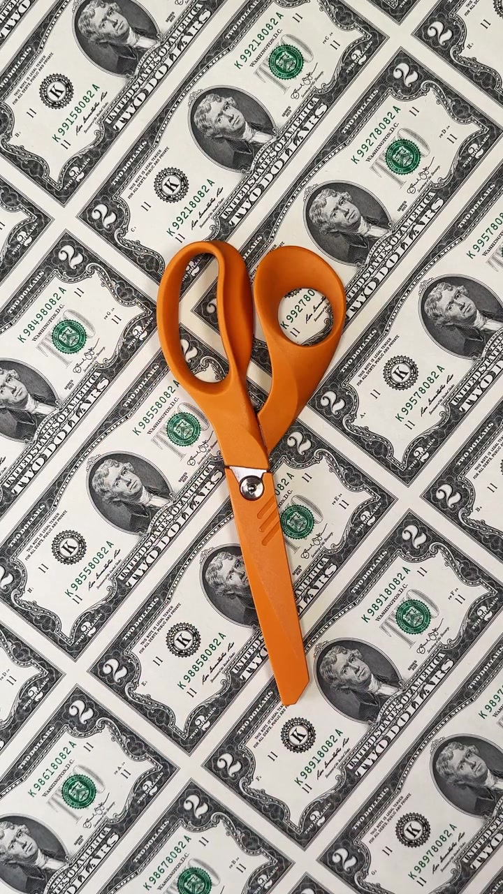 Scissors cutting souvenir dollar bills. Orange scissors cutting souvenir two dollar bills on printed sheet.