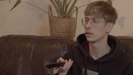 young man wearing glasses watches tv and changes channels