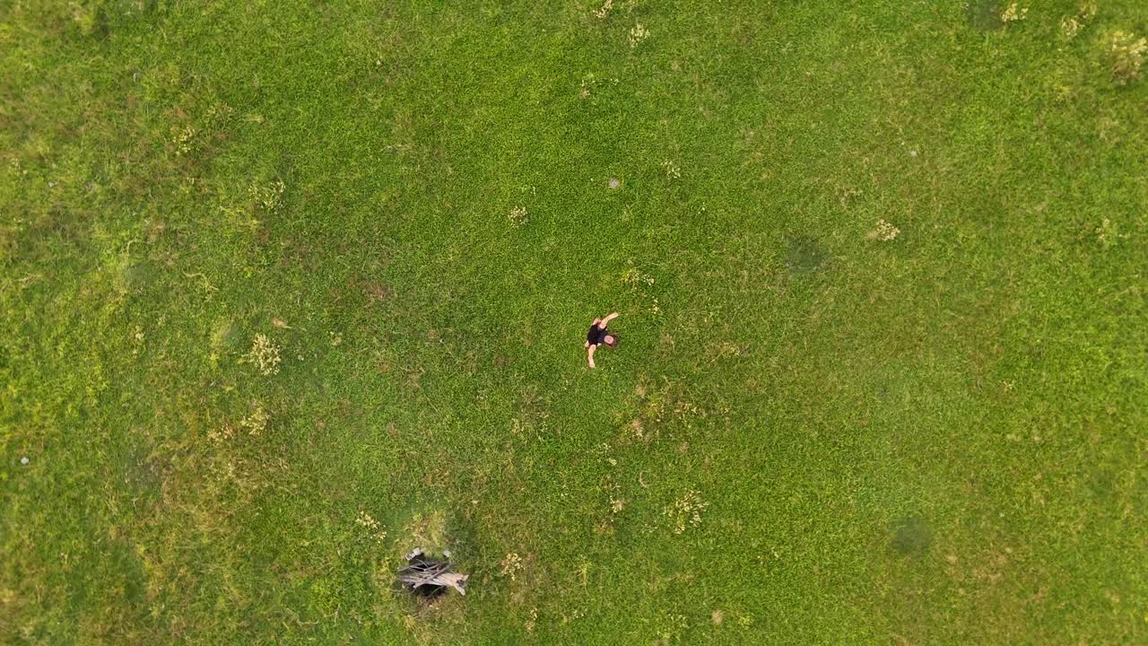 A dynamic rotating aerial shot capturing a woman gracefully performing headstand yoga pose on a lush grassy landscape.