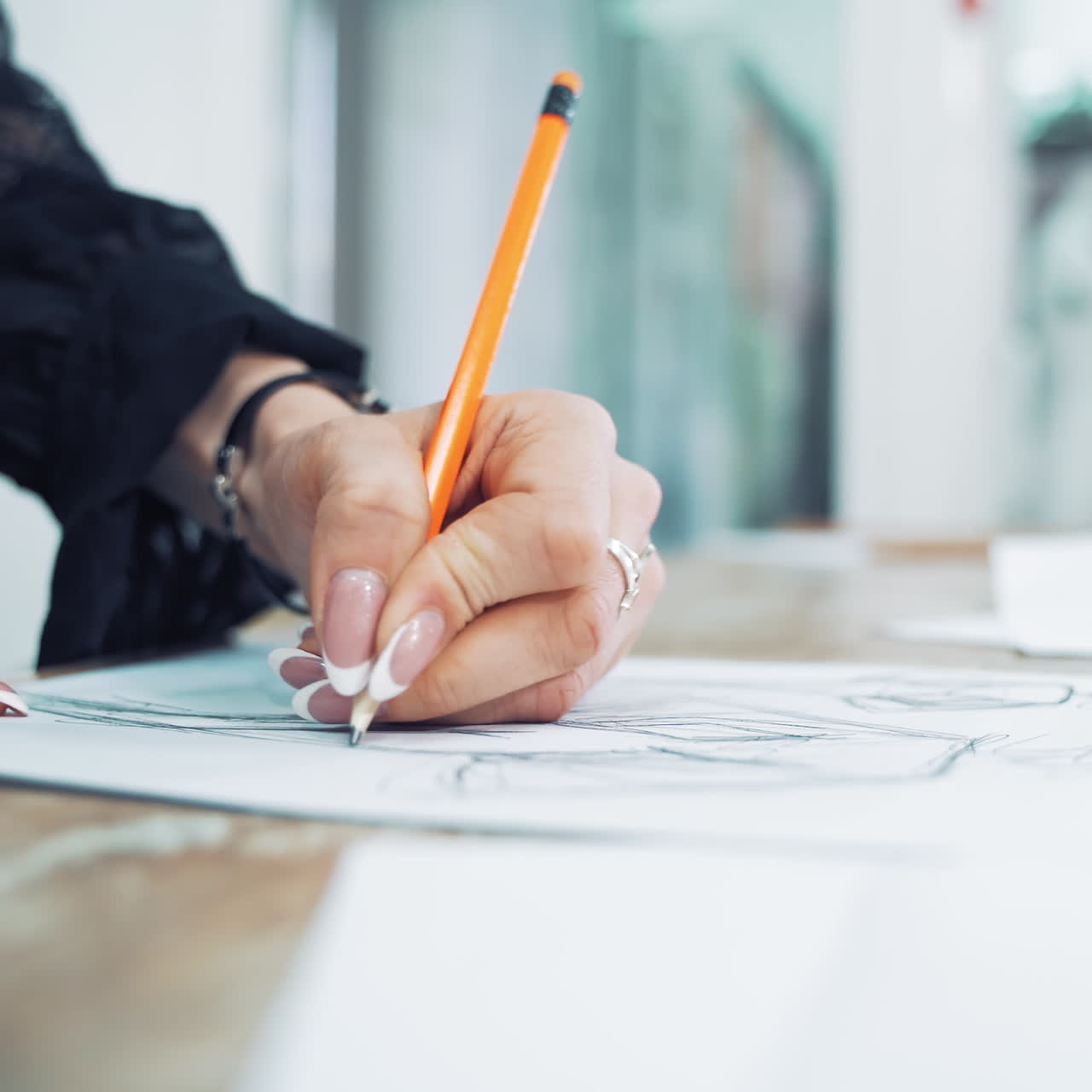Hands of a professional tailor is drawing a sketch with a sharp pencil on a table. Dressmaker is making a creative design of a dress on a sheet of paper in her workplace.