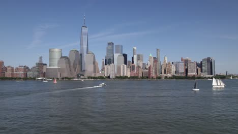 Aerial-view-over-boats-on-Hudson-river,-towards-the-Manhattan-skyline,-in-sunny-New-York,-USA---low,-rising,-drone-shot