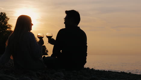 Silhouetten-Eines-Jungen-Paares,-Das-Wein-Bei-Sonnenuntergang-Am-Ufer-Des-Sees-Trinkt-3