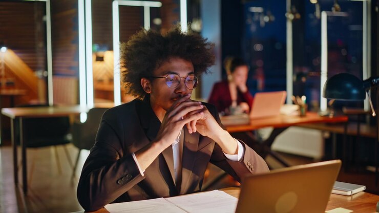 Imprenditore pensieroso che riflette mentre si mette gli occhiali in ufficio di notte. Uomo d'affari con laptop