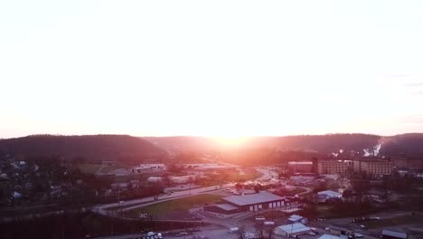 an aerial zoom pan of a beautiful golden sun setting over a small city area with a smoke producing bourbon distillery in the background