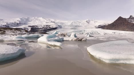 vatnajökull national park, iceland - stunning aerial drone flyover of fjallsárlón glacier lagoon with icebergs beneath towering snow-covered peaks and volcanic ridges.