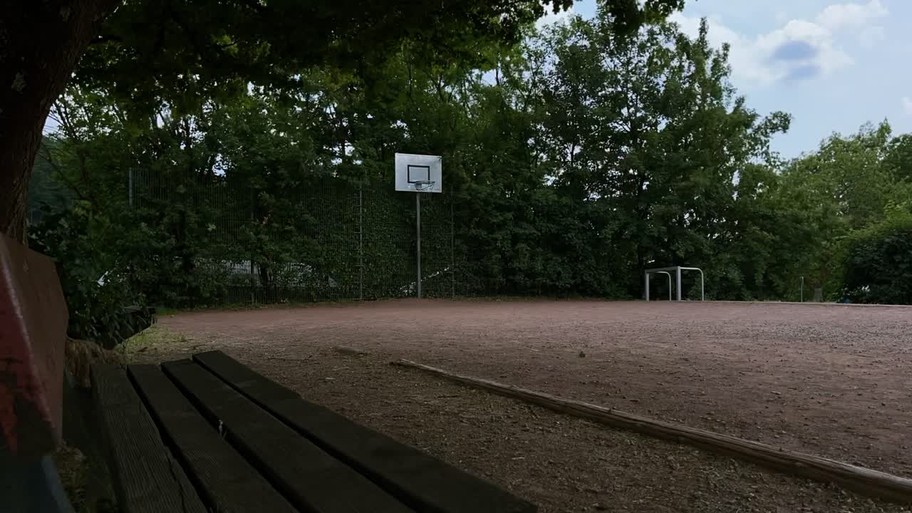 lapso de tiempo de un campo de baloncesto vacío con árboles en el borde de la acheplatz con algunos árboles cambiando sol y sombras