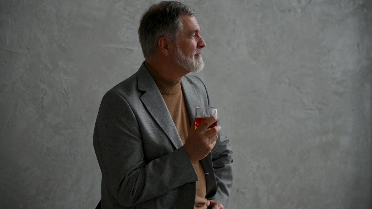 Zralý muž držící sklenici whisky u betonové zdi.