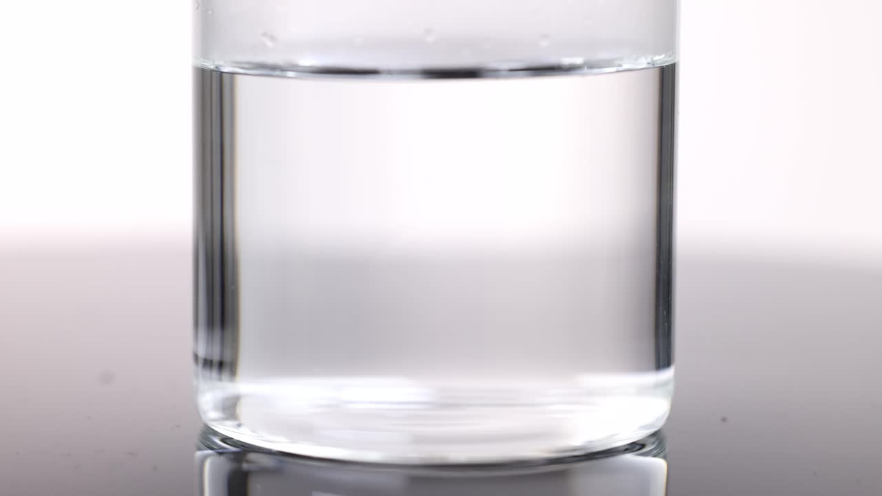 Effervescent tablet dropped into water, creating bubbles in a clear glass with bright lighting