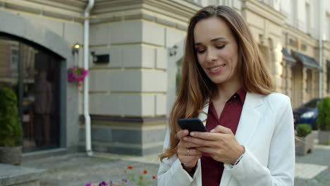 Glückliche-Geschäftsfrau,-Die-Draußen-Eine-SMS-Nachricht-Online-Auf-Dem-Smartphone-Sendet