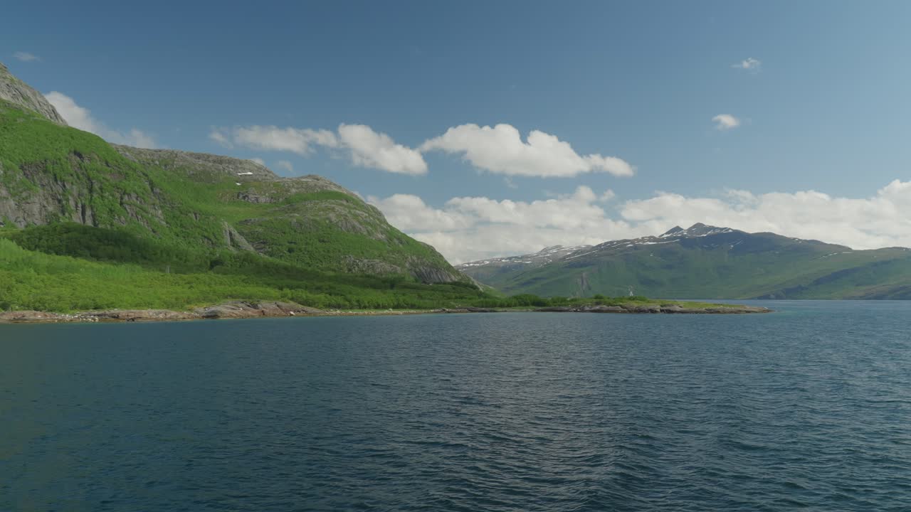 Scenic Fjord Landscape with Lush Green Mountains and Distant Snow-Capped Peaks under a Blue Sky