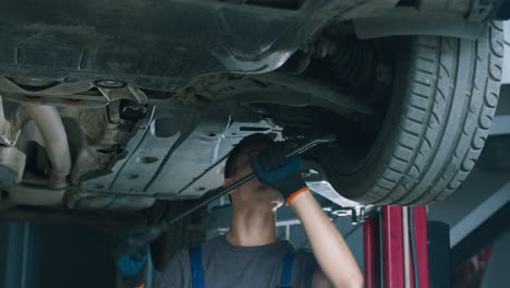 car mechanic working on a vehicle under lift