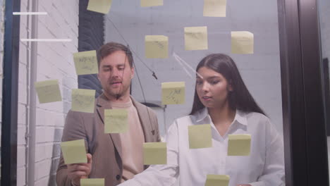 businessman and businesswoman brainstorming with sticky notes on glass window 2