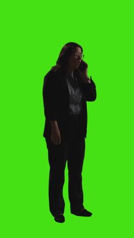 Vertikale-Videoaufnahme-Einer-Geschäftsfrau,-Die-Mit-Dem-Mobiltelefon-Vor-Einem-Greenscreen-Hintergrund-Mit-Schwacher-Beleuchtung-Telefoniert