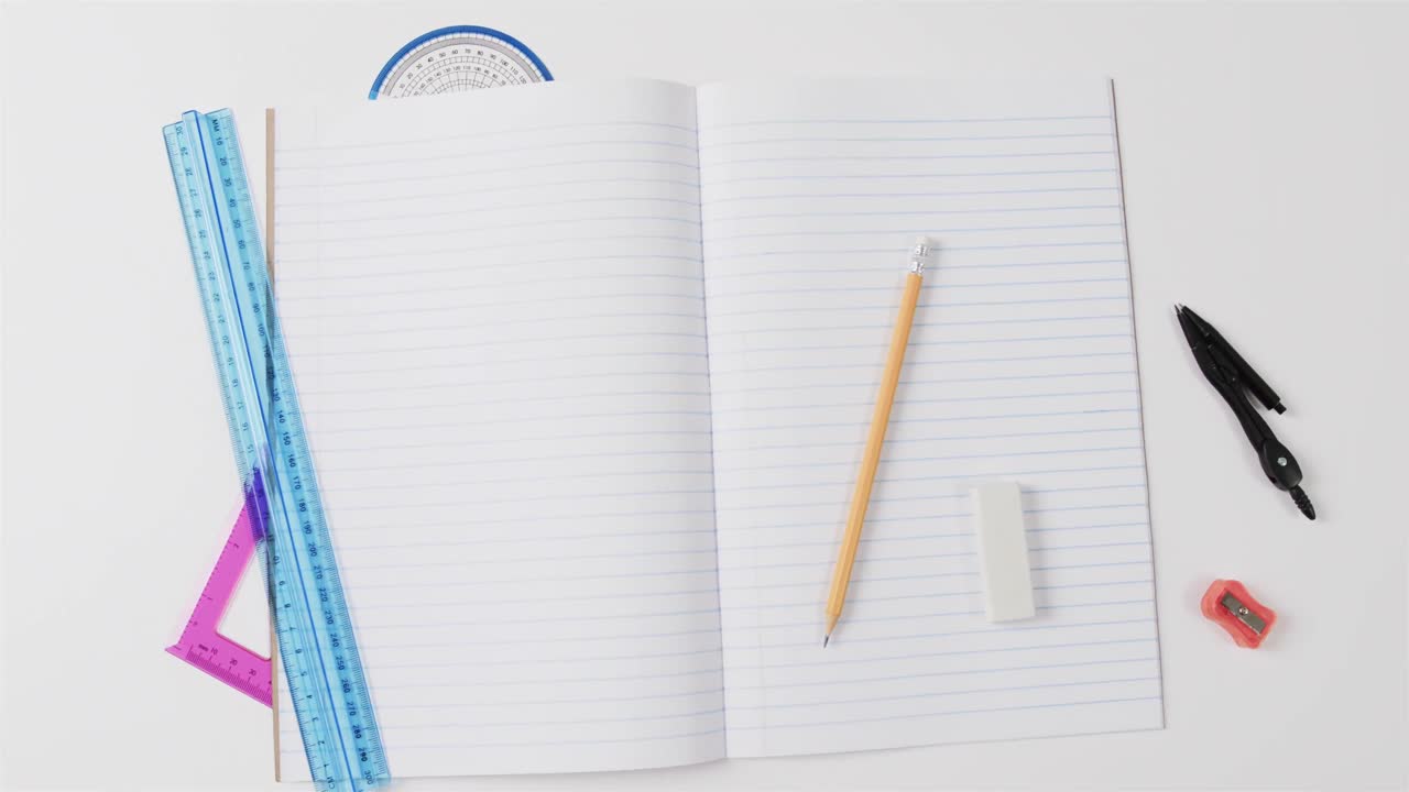 Overhead view of open notebook with school stationery on grey background, in slow motion