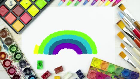 animación de dibujo de arco iris en un fondo plano de pintura con hoja de papel blanco, paleta de pinturas de acuarela, pinceles, crayones de tiza coloridos, telón de fondo para niños vista superior