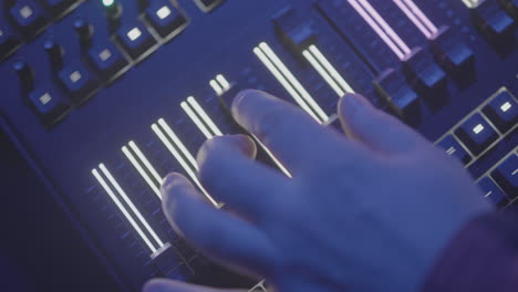 mano por encima de un panel de mezcla de audio o luz iluminado que se desliza hacia arriba y hacia abajo un control deslizante iluminado en cámara lenta en un registro de área de evento oscuro