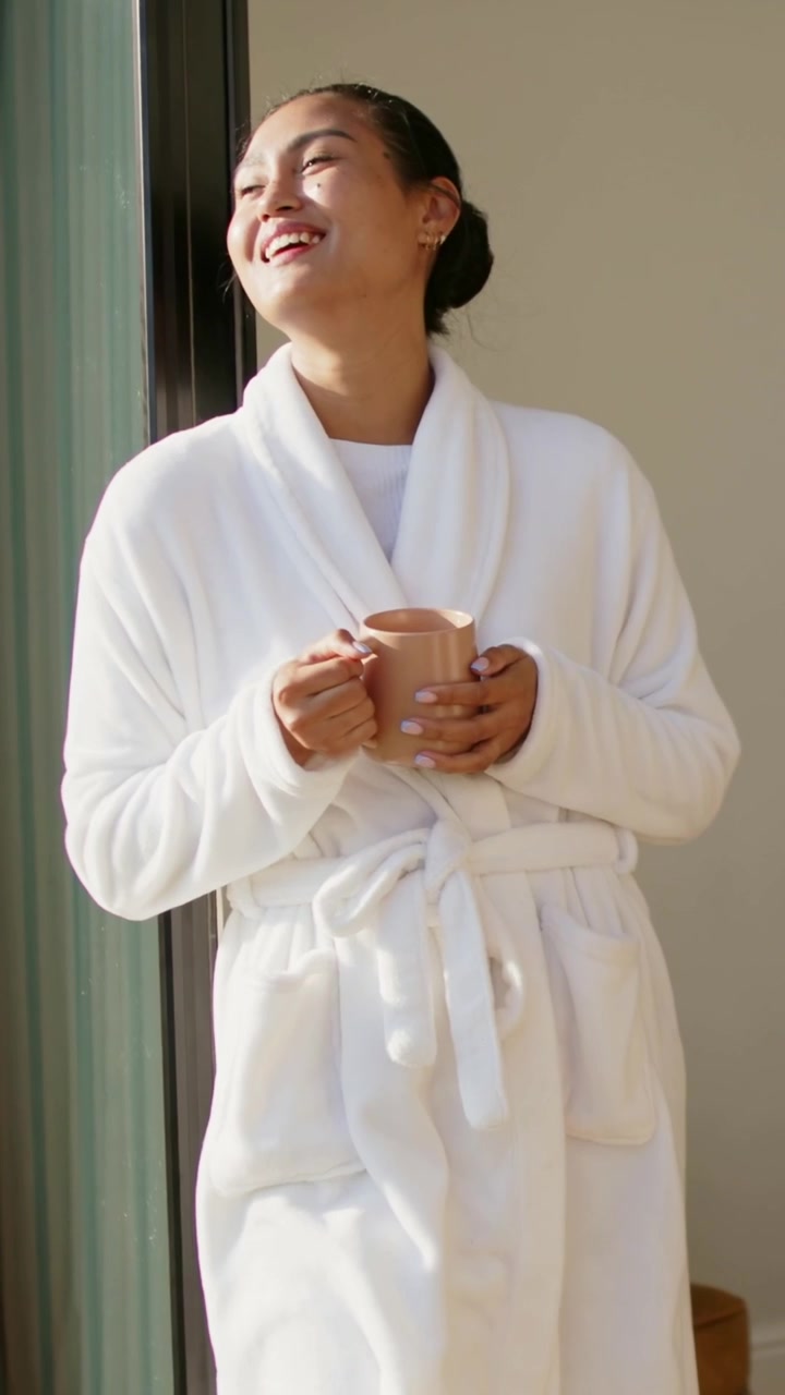 Vertical video: Holding beige mug, Asian woman spotting outside motion by sliding door in robe