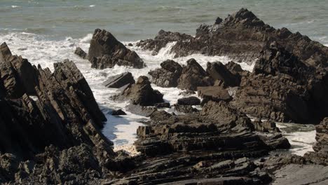 mid-shot-of-sea-breaking-and-crashing-over-jagged-sedimentary-rocks-in-the-Cornish-sea-at-Hartland-Quay,-Stoke,-Hartland,-Bideford