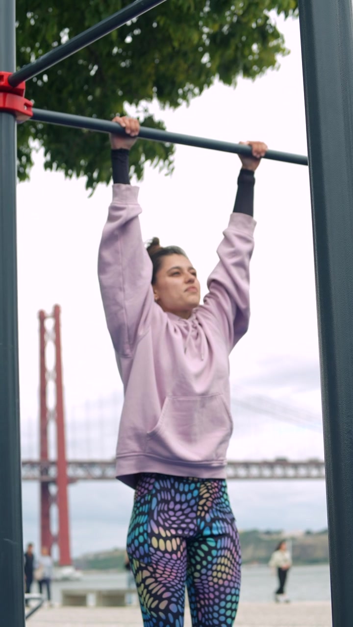 Young Woman Hanging on Pull-Up Bar at Outdoor Gym