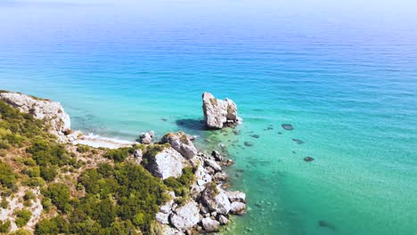 Tilt-up-aerial-drone-clip-moving-over-a-sandy-beach-and-a-rock-formation-in-Kavala,-Macedonia,-Greece