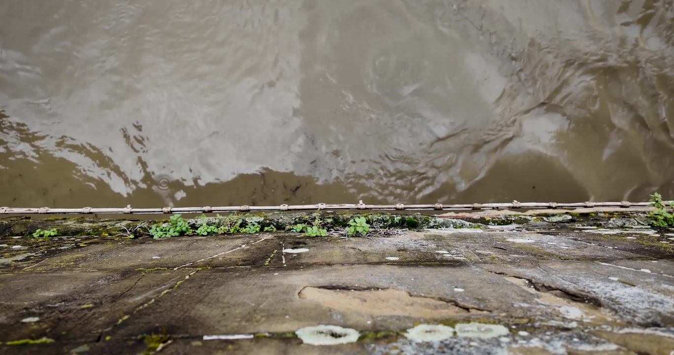 Top-down shot of the Arno River at Ponte Vecchio in Florence, Italy, with half the footage in slow motion, highlighting water flow, reflections and the iconic stone bridge structure.