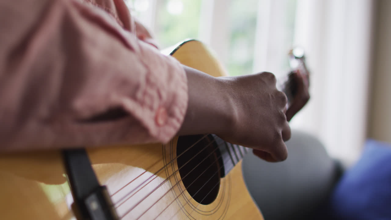 un primer plano de una mujer afroamericana tocando la guitarra en casa.