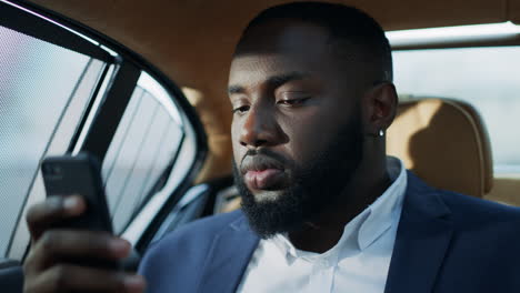 portrait of serious african man sitting at car. relaxed man looking phone screen