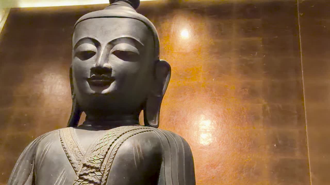 Un'inquadratura dal basso di una statua di Buddha in bronzo contro una parete luccicante di foglie d'oro.