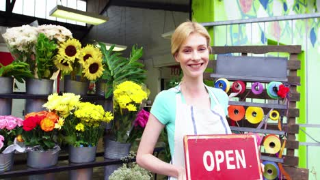 Smiling-florist-holding-open-sign-on-slate-in-flower-shop