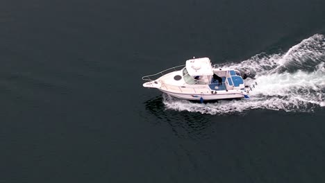 a white motorboat cruising along calm water at a fast speed - aerial follow