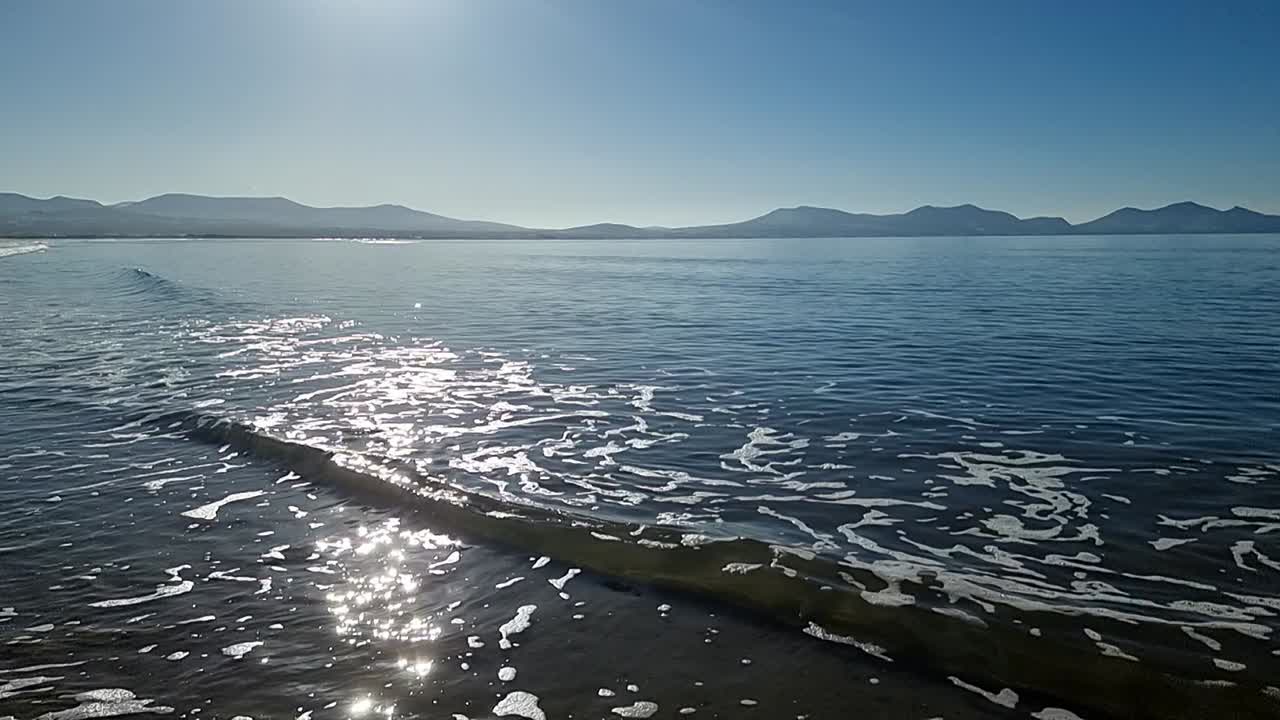 천상의 흐릿한 해가 뜨는 곳에서 느린 움직임의 조류 파도가 스노우도니아 산맥의 경치적인 스카이라인을  ⁇ 습니다.