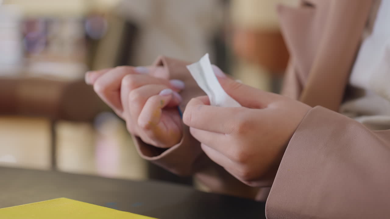 Primer plano de una mujer abriendo un regalo; toma detallada de una mujer curiosa descubriendo un regalo en una mesa de centro comercial; toma íntima que captura a una mujer de etnia caucásica desenvolviendo un pequeño regalo con curiosidad y ternura