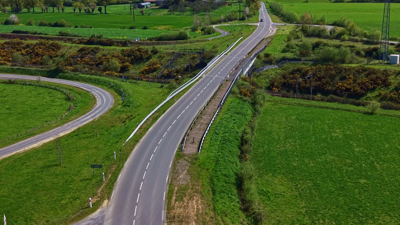 Dubbele rijbaan die een spoorwegcorridor kruist in het departement Mayenne, regio Pays de la Loire, Frankrijk, met autoverkeer en een coulisselandschap, drone voorwaartse glijvlucht luchtopname