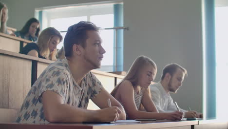 men and women students in ordinary clothes listen to a lecture in a large audience and write a lecture notes.