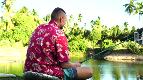 young adult fishing near small tropical lake with palm trees in background, back view