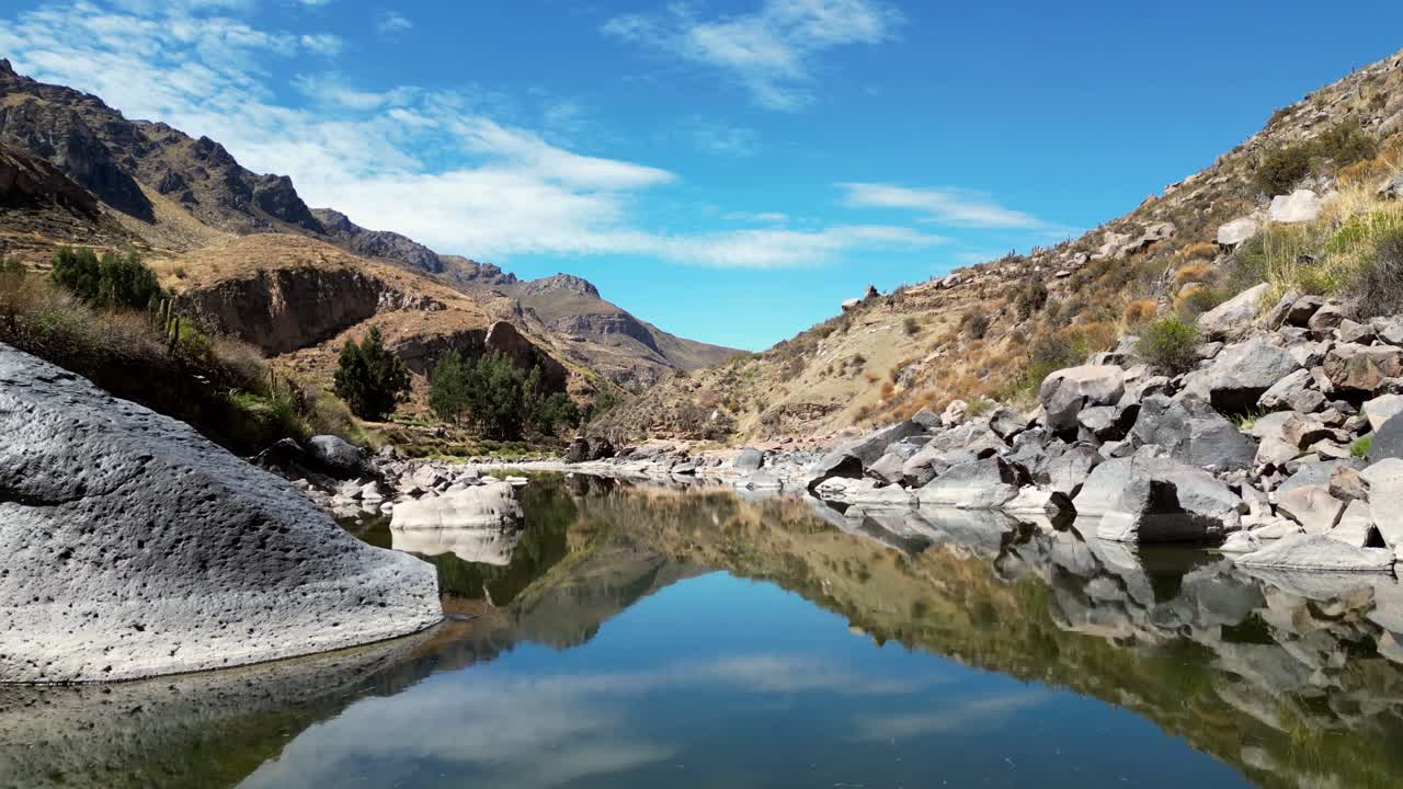 Low-altitude 4K drone footage following a river winding through the Peruvian Andes. The water reflects deep blue skies and golden light from the surrounding valley