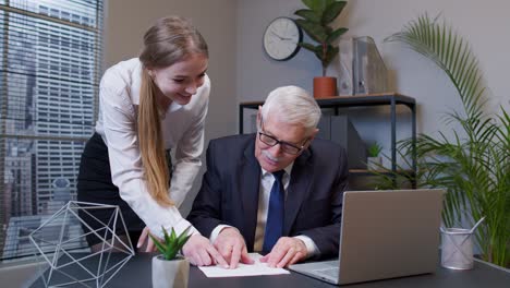 senior businessman examining financial data with woman colleague, celebrating good financial results