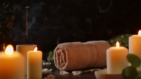 still life of lit candles with scattered petals incense stick and soft towels against dark background as part of relaxing spa day decor