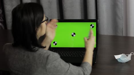 woman removes medical mask, take sanitizer and use near laptop with green screen