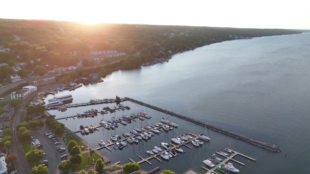 Scenic golden hour drone shot overlooking the boat marina on Seneca Lake at Watkins Glen. Aerial view of harbor docks catching the warm sunset light in the Finger Lakes region of New York.