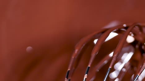 a detailed view of a whisk coated with glossy melted chocolate, highlighting its smooth texture and shine.