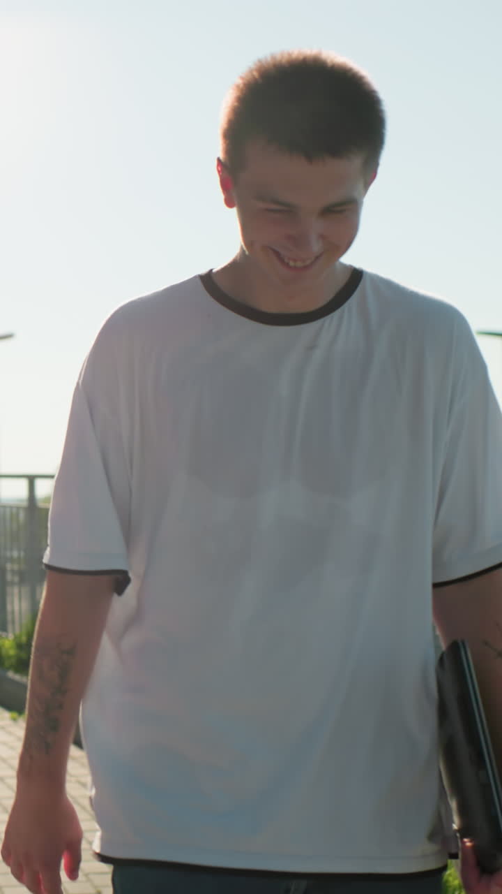 amigos caminando cerca de la barandilla de hierro, hombre con brazo tatuado conversando cálidamente con mujer sonriente sosteniendo un cuaderno, fondo que muestra vegetación y paisaje urbano expansivo bajo un cielo despejado