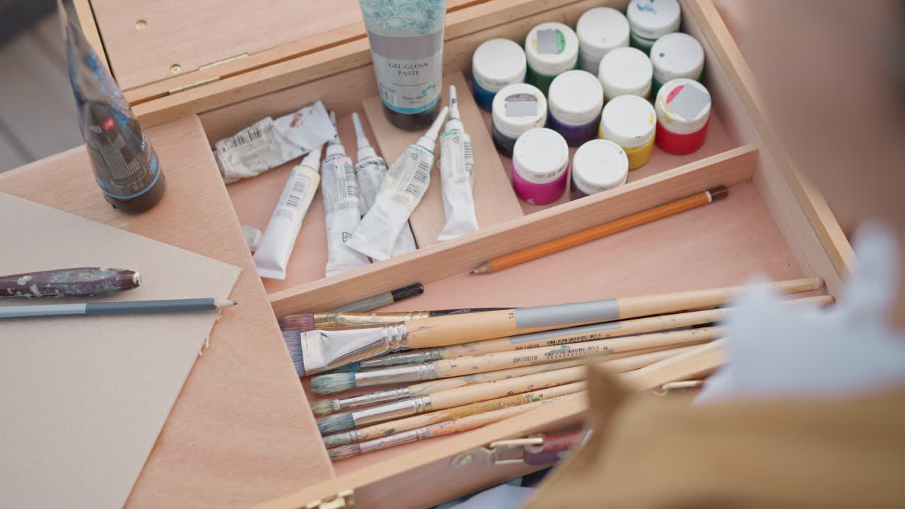 Tom skitsebog ved siden af malersæt på træbord med pensler, tuber med maling, krukker, palet. Urban sketcher arrangerer udstyr til gademalersession, nærbillede af tekstureret papir, penselgreb