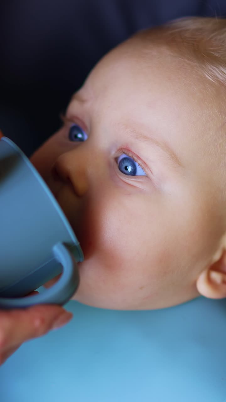 A un simpatico neonato caucasico viene data una tazza per bere. Primo piano. La madre sta dando da mangiare al suo bambino. Video verticale.