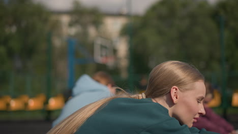 close-up of lady in green hoodie working out outdoors with two other ladies stretching in background, showcasing fitness, teamwork, and outdoor exercise in a sports arena